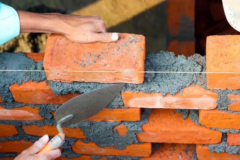 Hands laying a brick on fresh mortar with a trowel