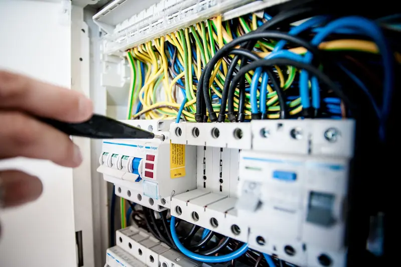 A hand testing wiring in an open fuse board