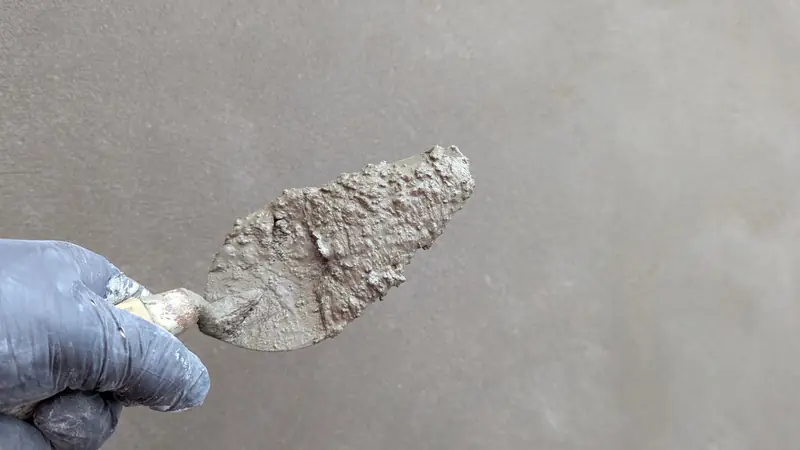 A gloved hand holding a plastering trowel against a wall